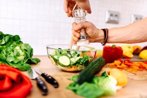 Close up details of adding salt and pepper to salad. handsome man in the kitchen Stock Photos