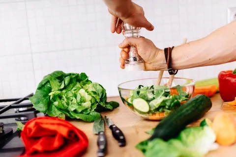 Close up details of a mens hands adding salt and pepper to salad Stock Photos