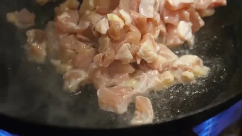 Close-Up of Diced Raw Chicken Breast Searing in a Hot Skillet on a Gas Stove Vídeos de archivo 347687871