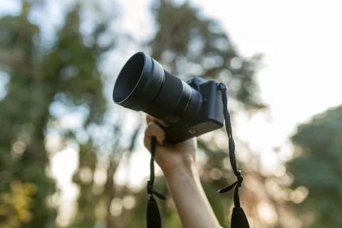Close-up of a digital camera held up by a hand outdoors, with soft bokeh Stock Photos