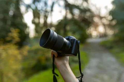 Close-up of a digital camera held up by a hand outdoors, with soft bokeh Stock Photos