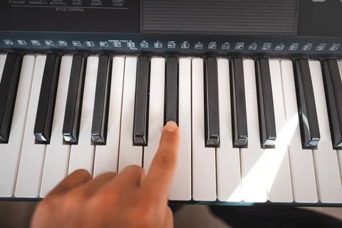 Close-up of a digital keyboard with a hand playing a melody, illuminated by s 스톡 사진