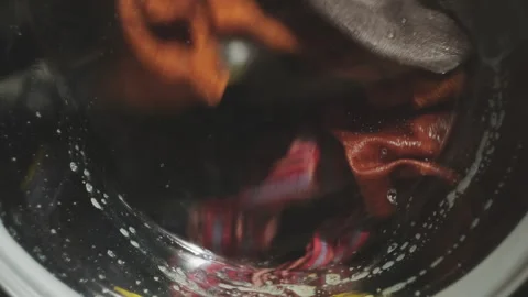 Close-up of dirty laundry spinning inside washing machine drum. Laundry service. Stock Footage 253673180