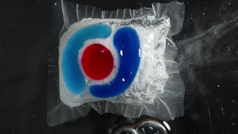 Close-Up of a Dishwasher Tablet Dissolving in Water, Releasing Blue and Red Stock Footage 283307596
