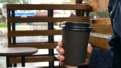 Close-up of a disposable paper cup for coffee is held by a woman hiding from the Stock Footage 169706700