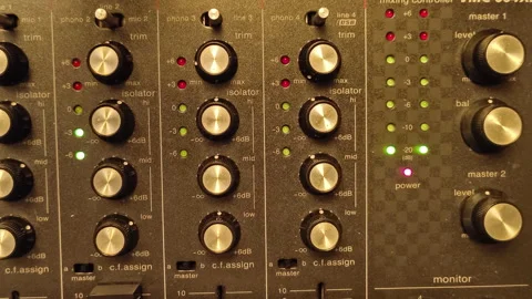 A close-up of a DJ mixer with numerous knobs, faders, and buttons, illuminated Video stock 300537538