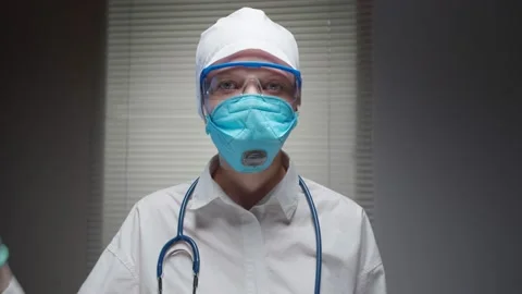Close up Doctor in front of the window with blinds, wearing a mask, gloves and Stock Footage 131271538
