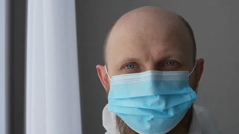 Close-up of a doctor's face in a surgical mask. A bearded medic takes off his Stock Footage 172248128
