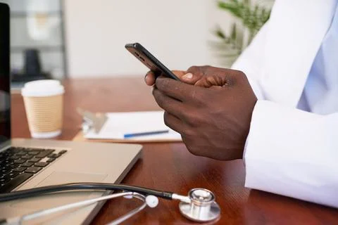 Close up of doctor's hands using cellphone at desk in office, stethoscope Stock Photos