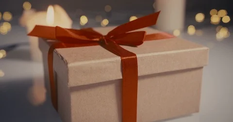 Close-up dolly shot of a simple gift box on a bokeh background with lit candles Stock Footage 100875198