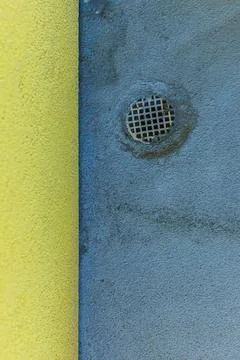 Close-up of a drain on a blue painted surface with yellow wall Stock Photos
