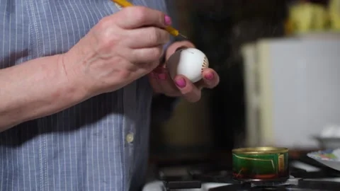 Close up drawing patterns with wax with a pencil on an egg near a stove by woman Video stock 131041835