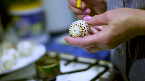 Close up drawing patterns with wax with a pencil on an egg near a stove by woman Stock Footage 131043248