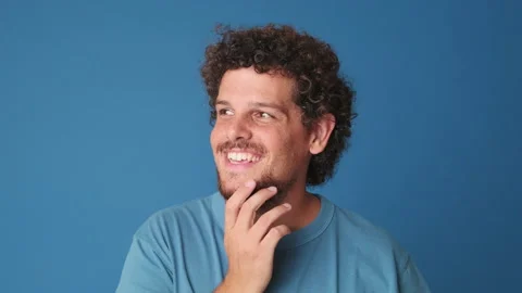 Close up, dreaming man looking at the camera with smile, isolated on blue Video stock 252502380