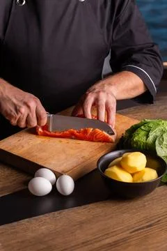 Close-up of dressed in black chef cuts with knife the salmon at the professio Stock Photos