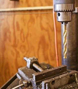 Close up of a Drill Press With Gold Colored Drill over Vice Фото