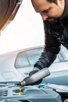 Close-up driver hand holding small bottle can pouring synthetic motor oil in 스톡 사진