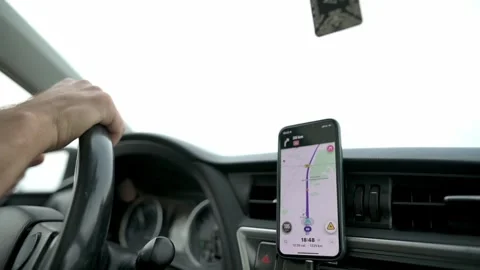Close-up of a driver hands on the steering wheel and a smartphone mounted on the Vidéo 281018334