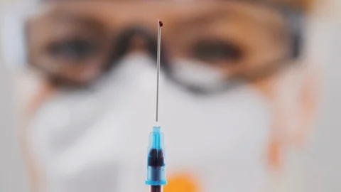 Close-up drop of blood on the tip of a needle. Blurred face of woman doctor Stock Footage 128373385