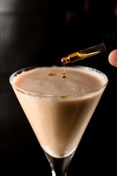 Close-up of drop of falling out of dropper in martini glass with a cocktail Stock-Fotos