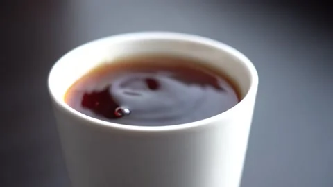 Close-up of a drop falling into a white mug with black tea Stock Footage 147314912