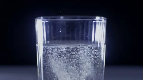Close-up of dropping a round white tablet into a glass of water Stock Footage 75546916