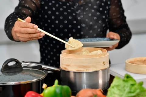 Close up of a dumpling being picked up from a bamboo steamer by a female hand Stock Photos