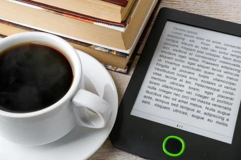 Close-up of e-book reader near cup of hot coffee and stack of paper books. Stock Photos