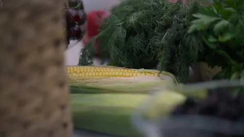 Close-up ear of corn lying on table with female hands putting tomato and Stock Footage 169515343