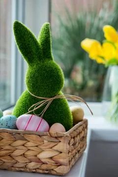 Close up Easter bunny rabbit in straw basket with colored eggs on the windowsill Stock Photos