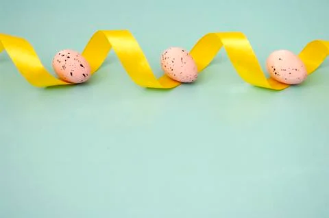 Close up easter quail pink eggs with yellow ribbon on pastel blue background. Stock Photos