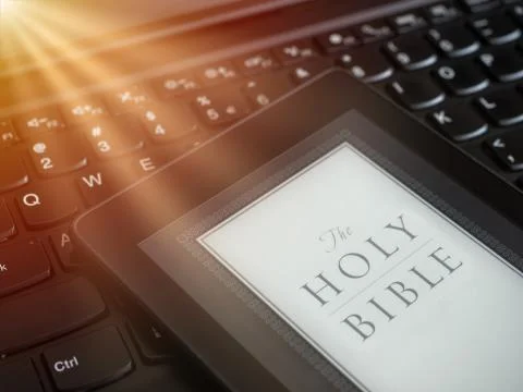 Close up of ebook reader with The Holy Bible on a laptop keyboard, with sun r Stock Photos