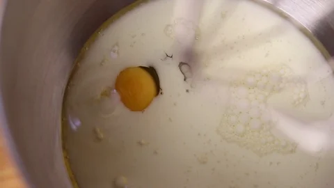 Close-Up of egg being added to oil and milk in mixing bowl Stock Footage 129329718