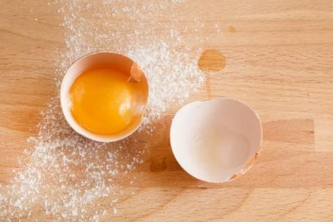 Close up egg, yolk in eggshell, flour on a wooden background Stock Photos
