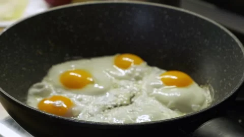 Close-up of eggs frying on a black pan Stock Footage 232680417