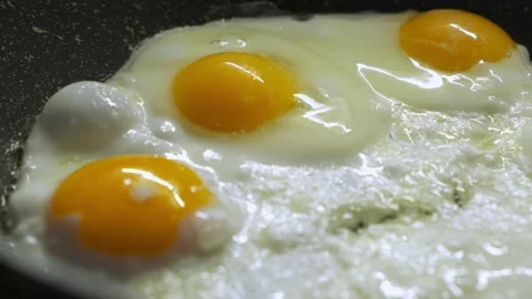 Close-up of eggs frying on a black pan Stock Footage 232680429