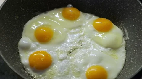 Close-up of eggs frying on a black pan Stock Footage 233903770