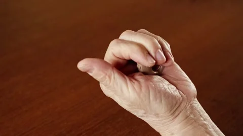 Close-up of an elderly hand holding a beige hearing aid on a wooden table. Stock Footage 310607673
