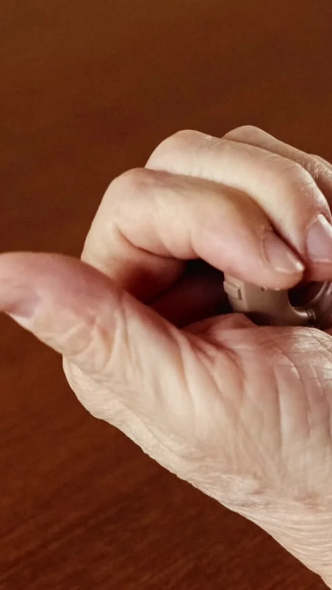Close-up of an elderly hand holding a modern hearing aid on a wooden table. Stock Footage 312378250