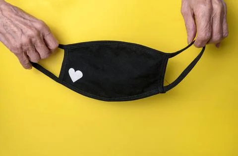 Close-up of elderly hands holding a handmade black mask on a yellow backgroun Stock Photos