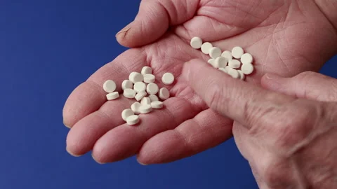 Close-Up of Elderly Hands Holding White Pills on Blue Background Stock Footage 304394736