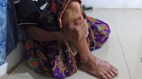 Close-up of an elderly Indonesian man sitting indoors, rubbing his legs and feet Stock Footage 321932916