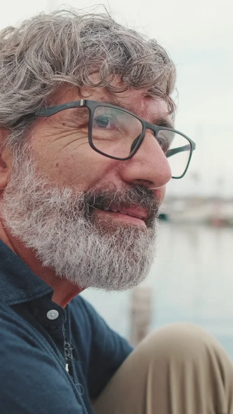 Close-up of an elderly man sitting on pier in marina and listening attentively Stock Footage 253935954