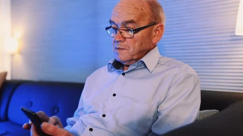 Close up of elderly man sitting in a sofa at night typing on his smart phone Stock Footage 99014815