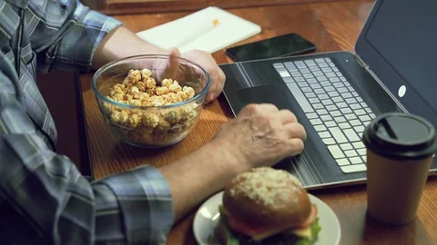 Close up of an elderly man's hands holding a bowl of popcorn working on a laptop Stock Footage 128222879
