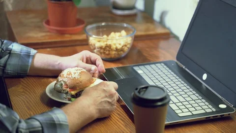 Close-up of an elderly man's hands holding a Burger watching a movie on a laptop Stock Footage 128224983
