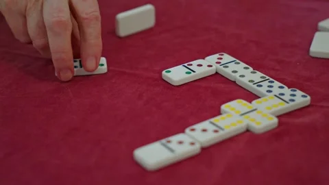 Close-up of an elderly person placing a domino tile during a game on a red felt Stock Footage 337690871