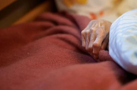 Close up of an elderly person's hand gripping a red wool blanket while lying  库存照片