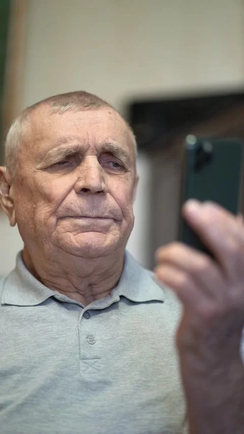Close-up of elderly senior man holding phone and viewing screen content indoors Vídeos de archivo 346176328