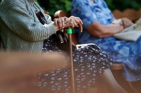 Close up of an elderly woman's hands resting on a wooden walking stick while  Фото
